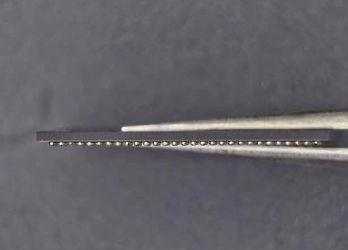 Side profile view of a BGA chip held by tweezers, highlighting the coplanarity and uniformity of the solder balls.