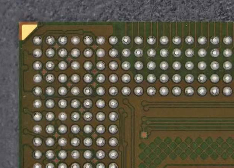 High-magnification macro shot of a BGA chip corner showing individual solder balls, substrate traces, and via holes.