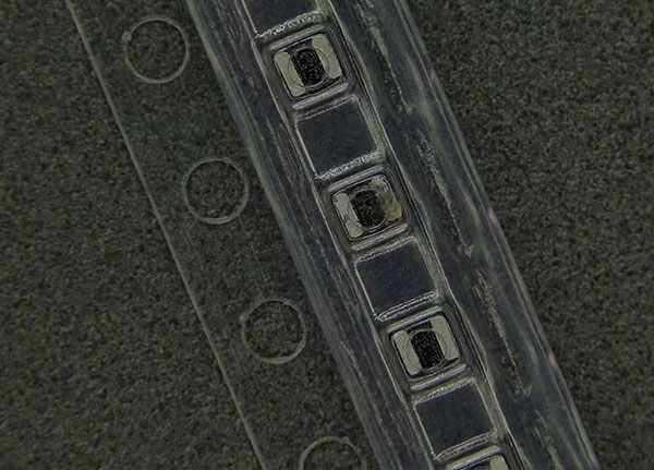 Macro view of surface mount electronic components sitting securely inside clear plastic carrier tape packaging.